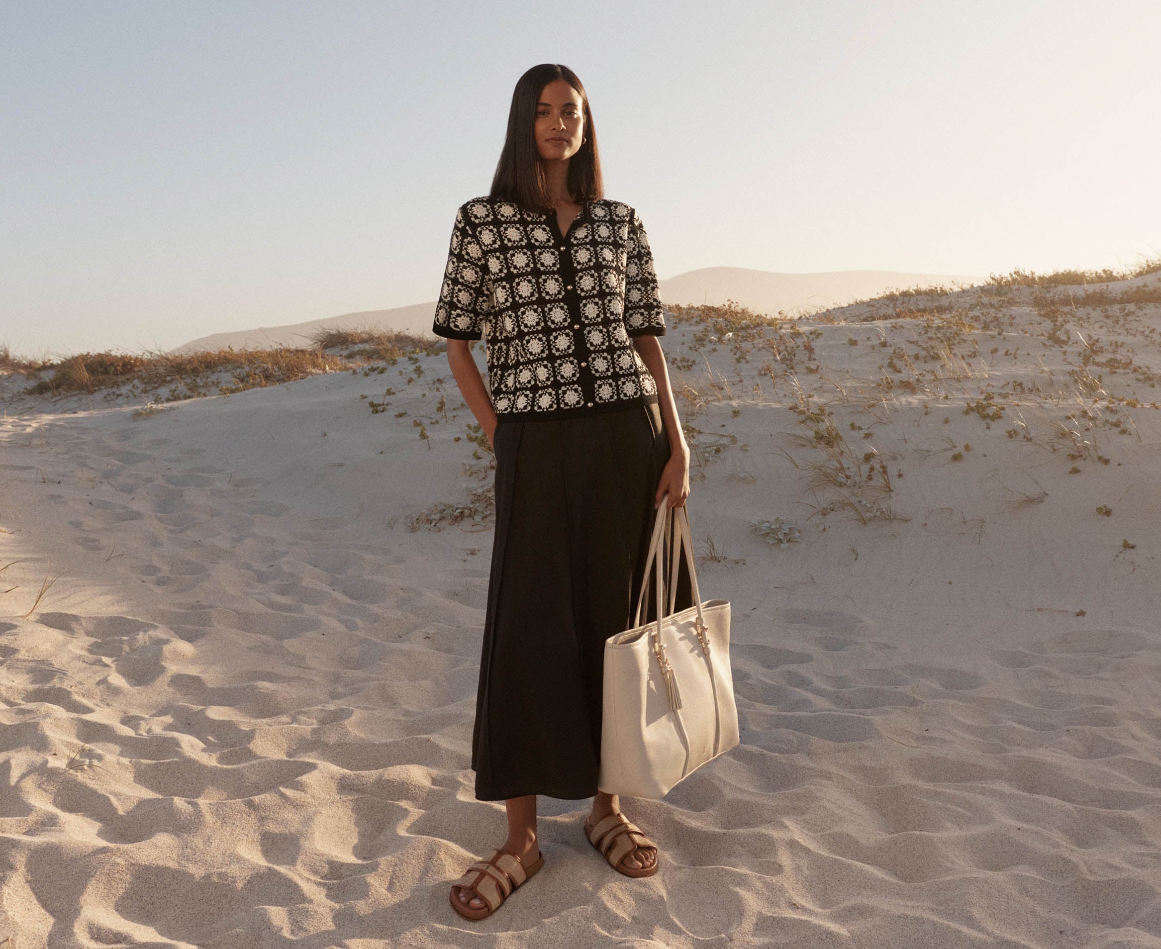 A woman wearing a monochrome summer outfit and leather tote bag.