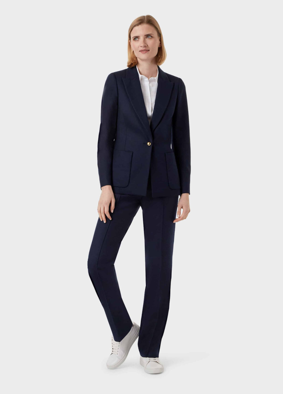 Women’s blazer in black worn with matching work trousers in black, with a white blouse underneath and white trainers, by Hobbs.