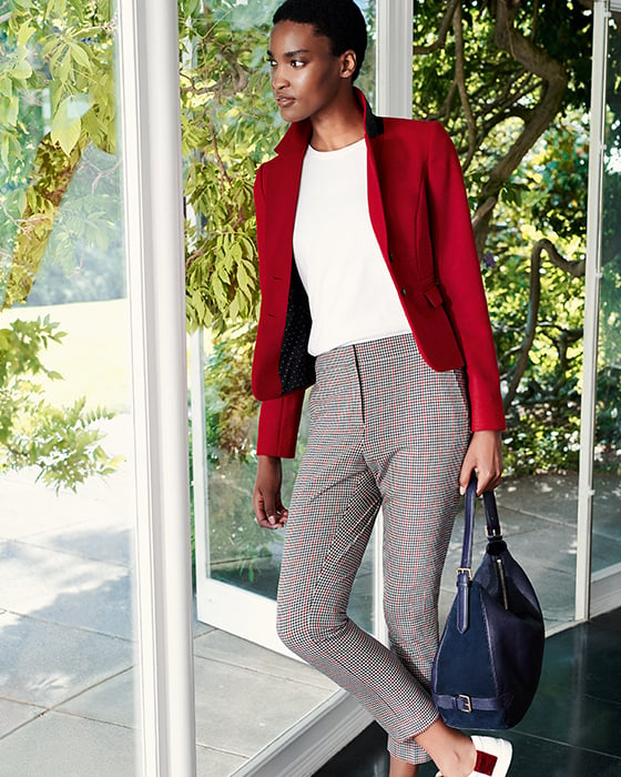 Model wears a bright red wool jacket, tailored trousers, white leather trainers with a blue leather bag