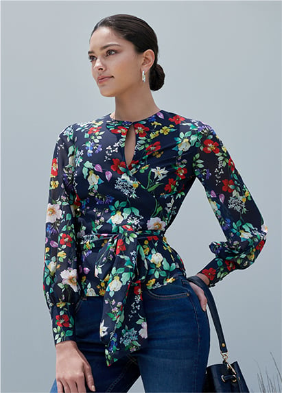 Woman poses in a navy blue floral wrap top styled with jeans and a navy blue leather hand bag