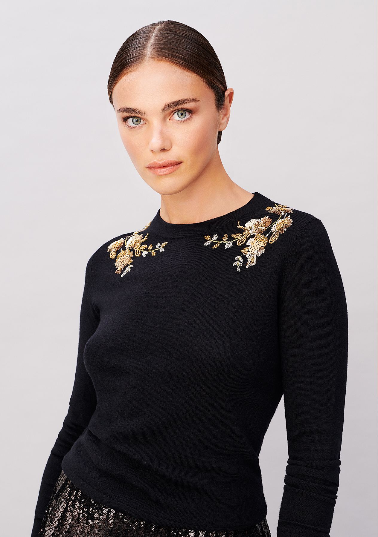 Close-up image of model wearing a black jumper with a gold embellished neckline.