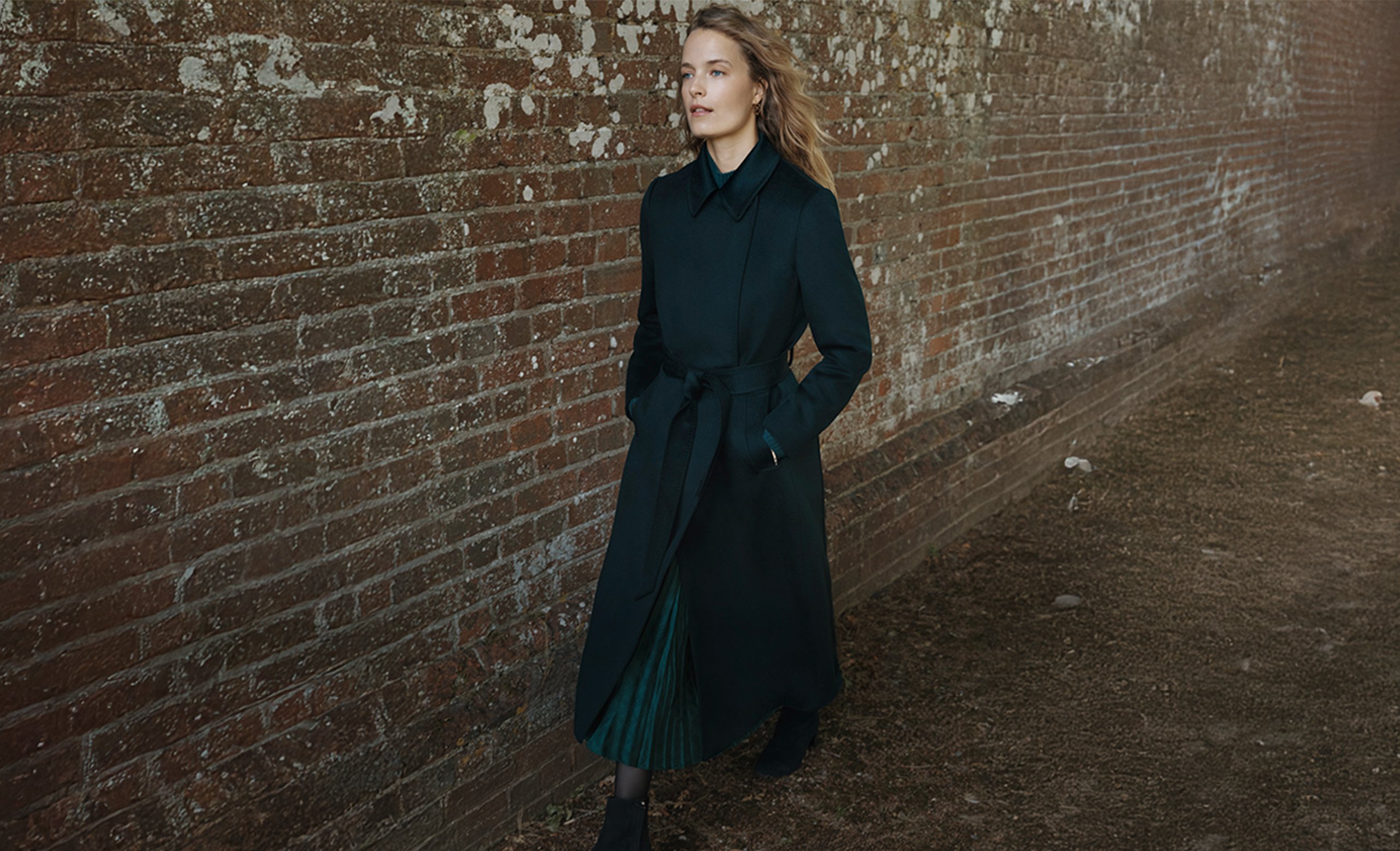 A woman wearing a teal wool coat over a teal midi skirt.