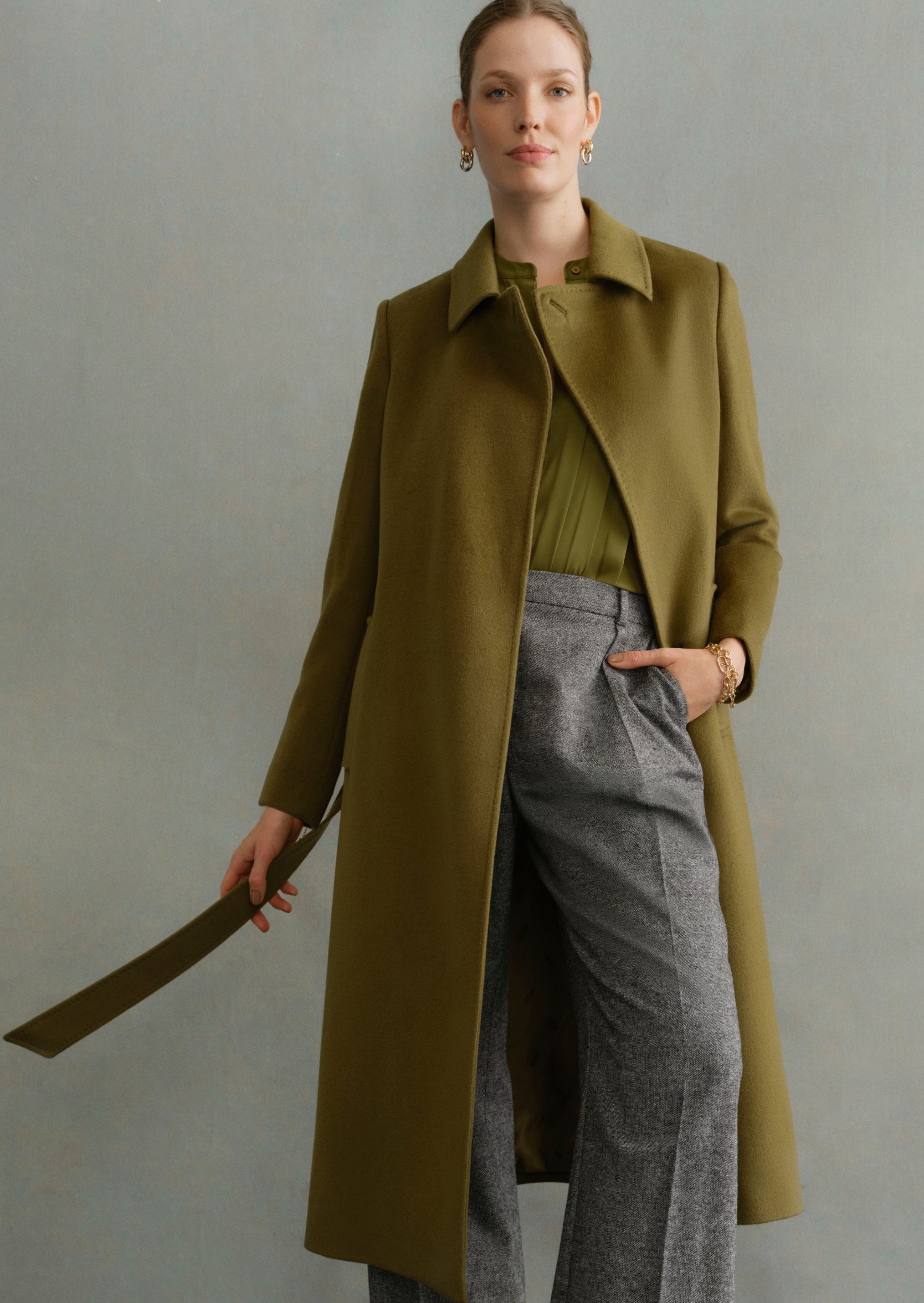 Image of a model wearing an olive green tailored coat over smartwear.
