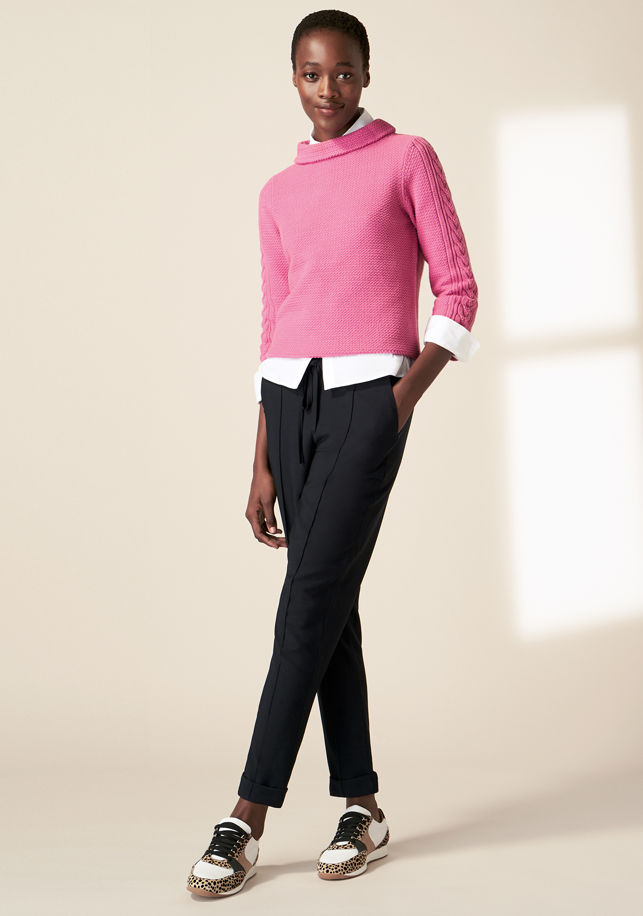 Model photographed wearing a pink knitted jumper with navy joggers and trainers.