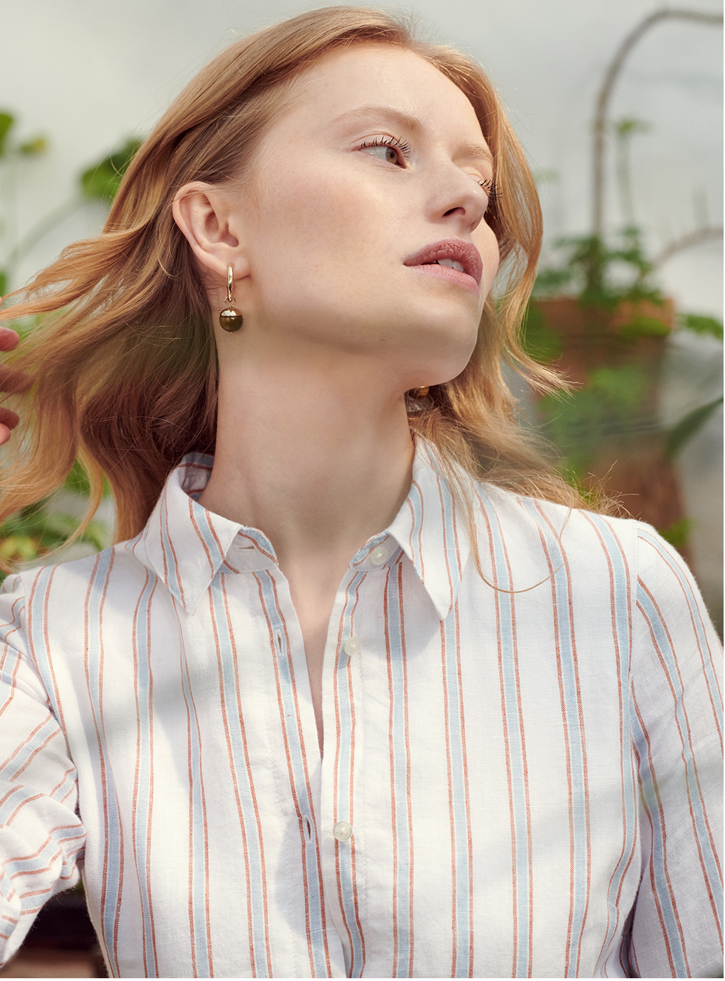 Model in a striped shirt dress wears a pair of earrings.