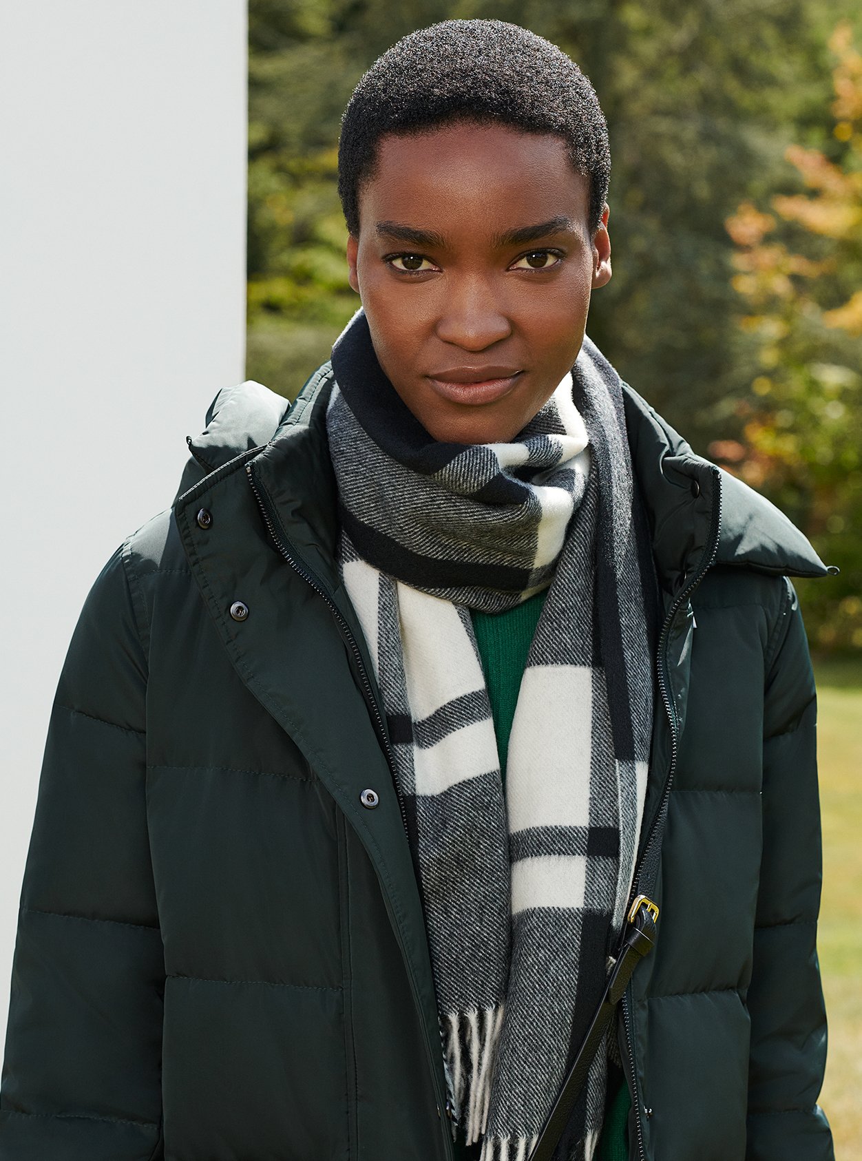 Close-up of model in a garden wearing a puffer coat and checked scarf.