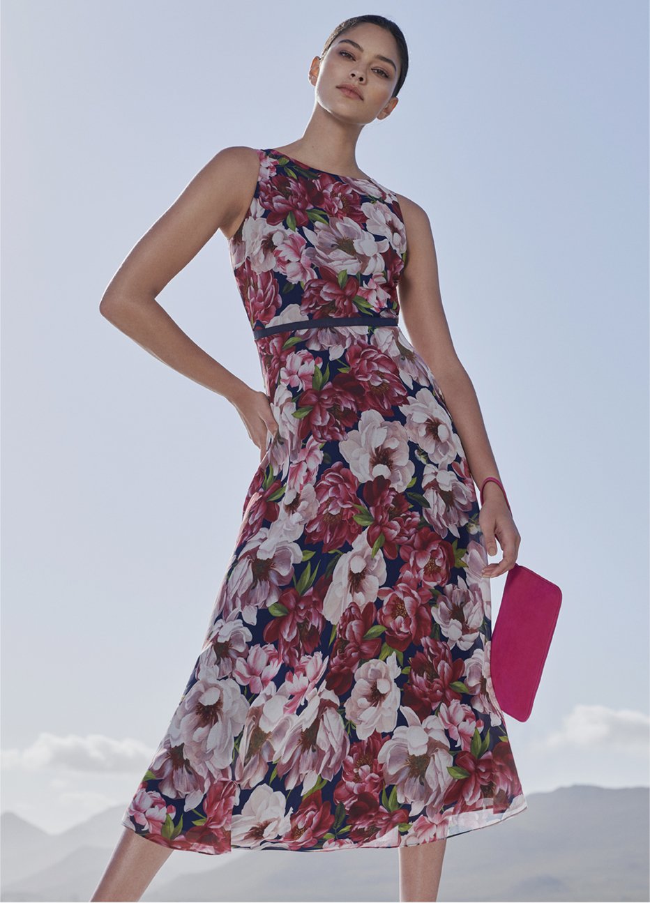 Midi-length occasion dress with a pink floral pattern paired with a pink wristlet clutch and flat shoes by Hobbs.