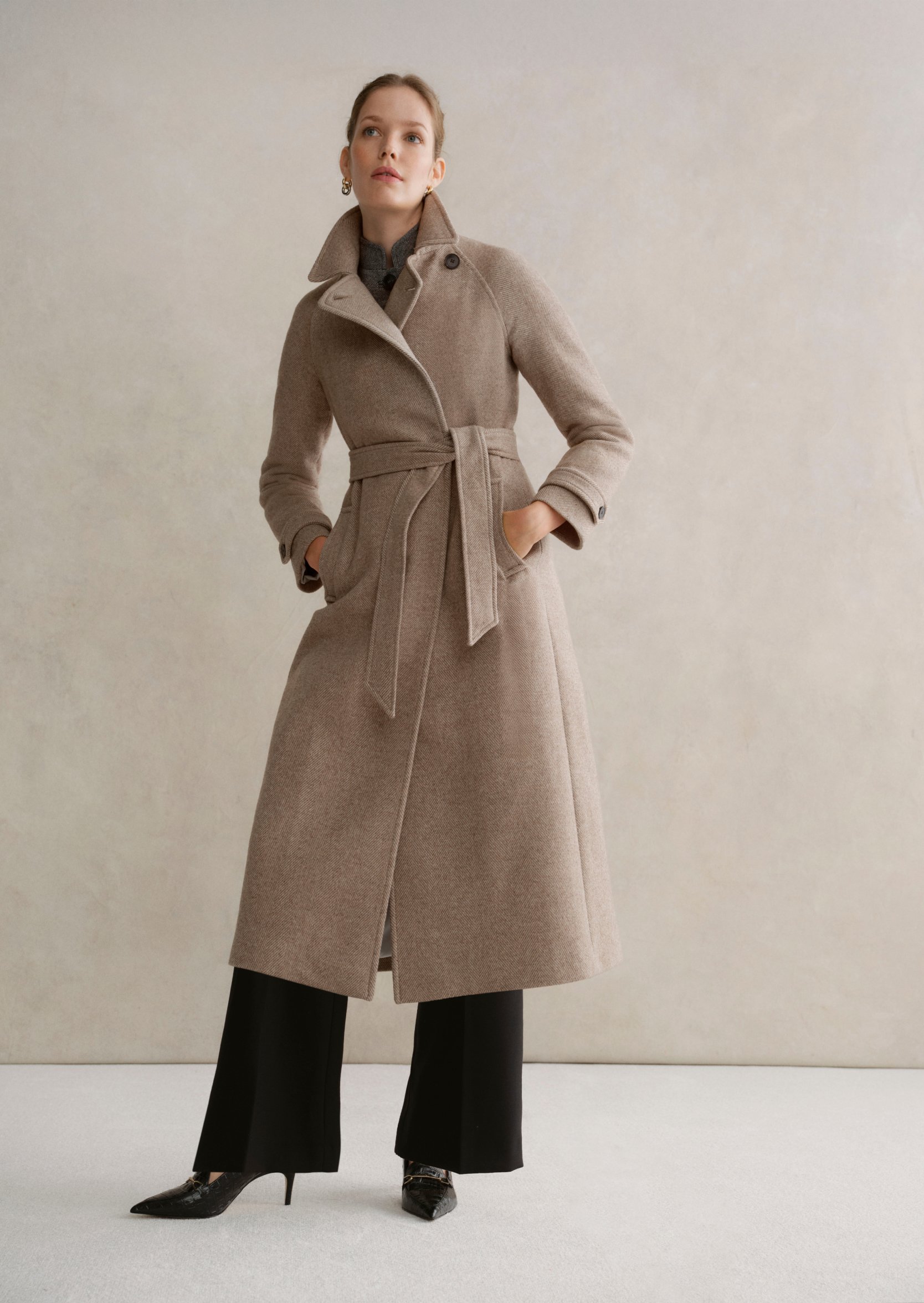 A gallery of two images displaying a model wearing a beige tailored coat.