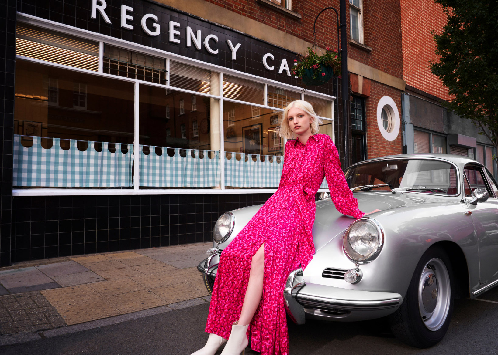 Model photographed lounging on a silver car wearing a pink patterned shirt dress.