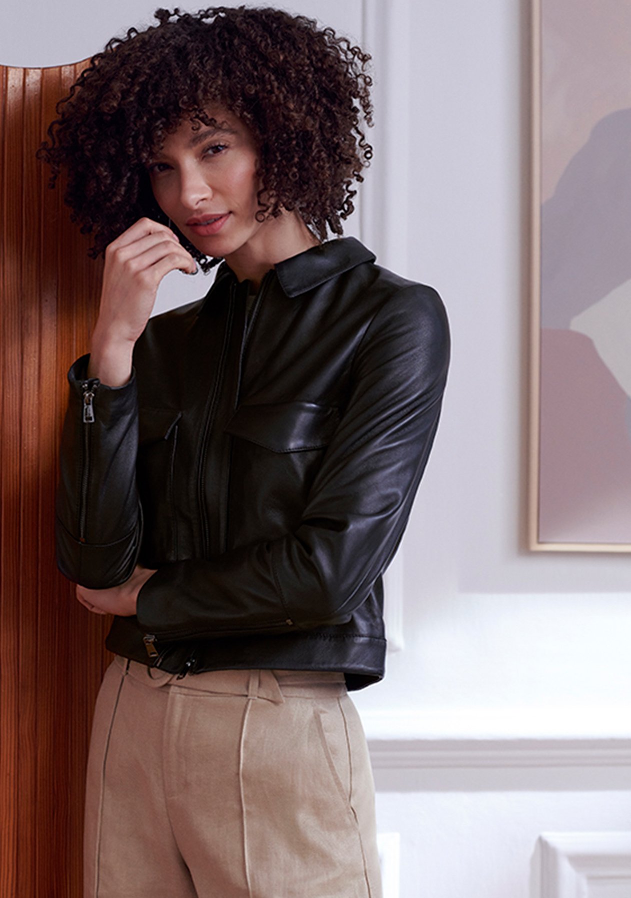 Model photographed wearing a green satin blouse with black trousers and a clutch bag.