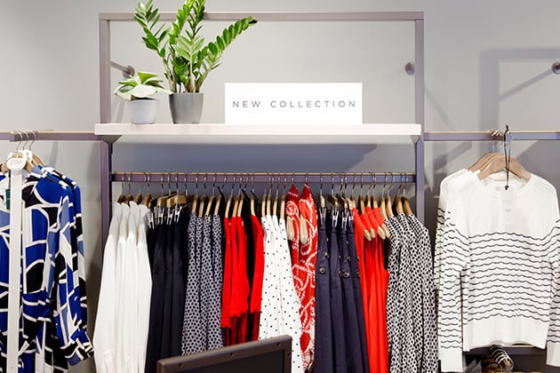 An image showing a section of a shelf in a Hobbs store. The shelf is decorated with a piece of framed artwork, a new collection sign, wrislets in blue, green, pink and white, court shoes in blush pink, and the upper half of a few hung up garments which include a dotted shirt in black and white, a polka dot top in black and white placed next to other designs in white, black and pink.