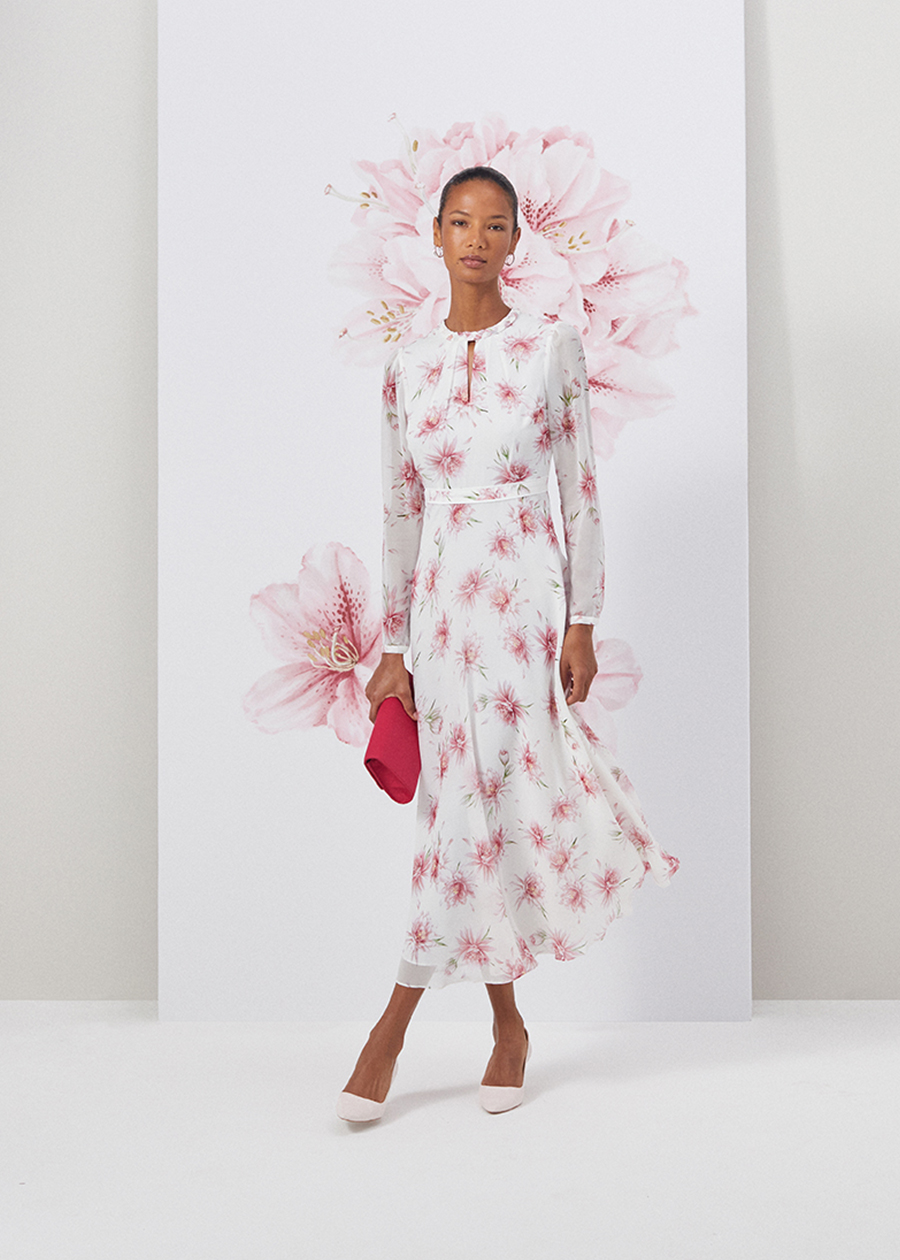 Image of model standing in front of a floral painted background wearing a navy floral print silk midi length dress.