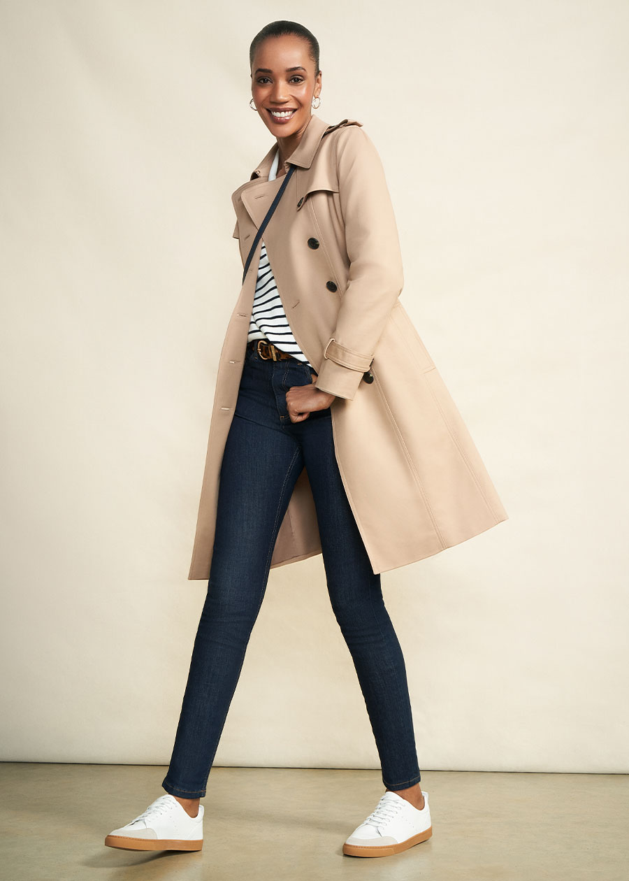 Model photographed against a canvas background wearing Hobbs Saskia trench, a striped jumper, dark wash jeans and trainers.