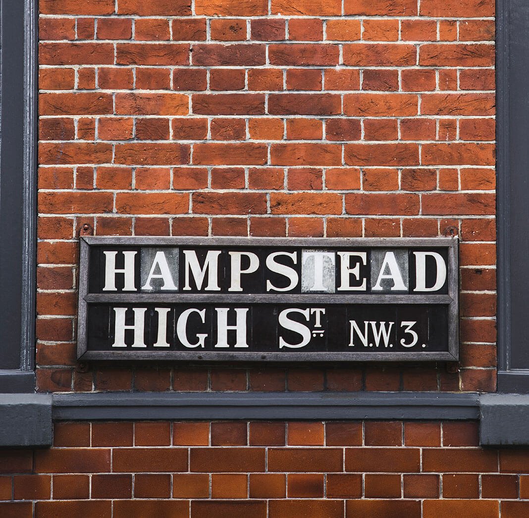 Photograph of a street sign on the side of a building reading Hampstead High Street.