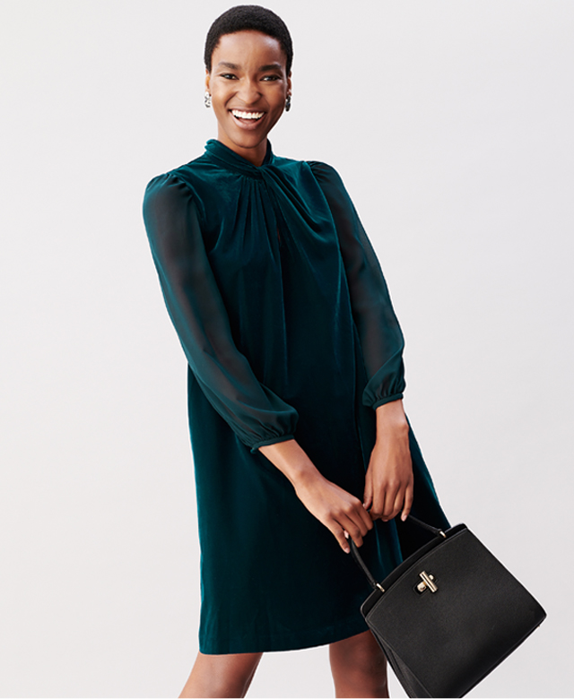 Model photographed wearing a dark green velvet dress holding a black bag.