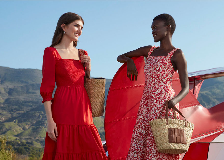 Image of two models in front of an aeroplane wearing open toe sandals, summer dresses and woven tote handbags.
