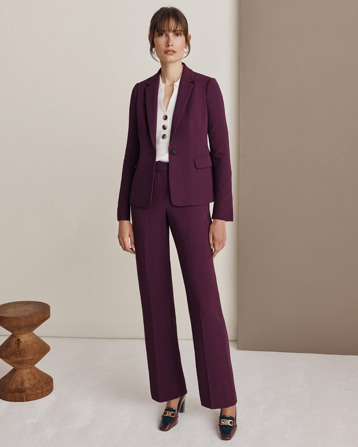 Model photographed against a neutral backdrop wearing a Hobbs burgundy suit with matching coat draped on her shoulders.
