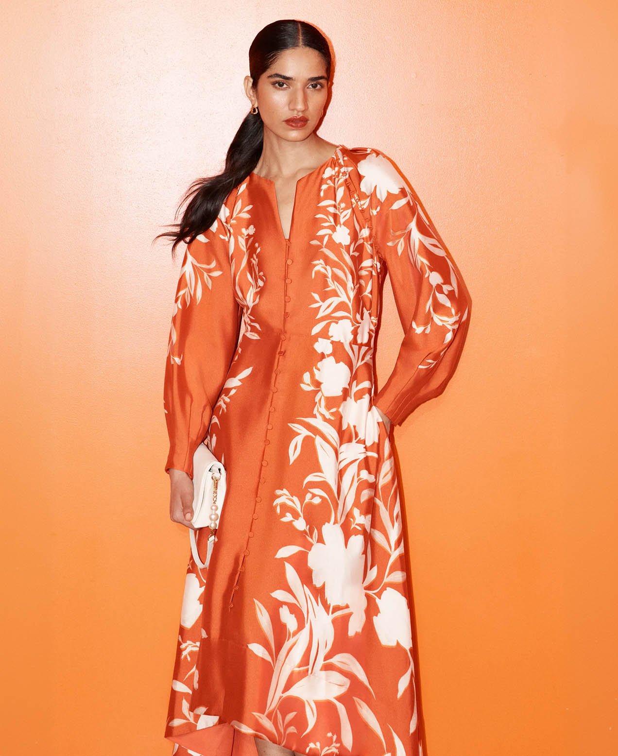 A woman wearing an orange, floral occasion dress.