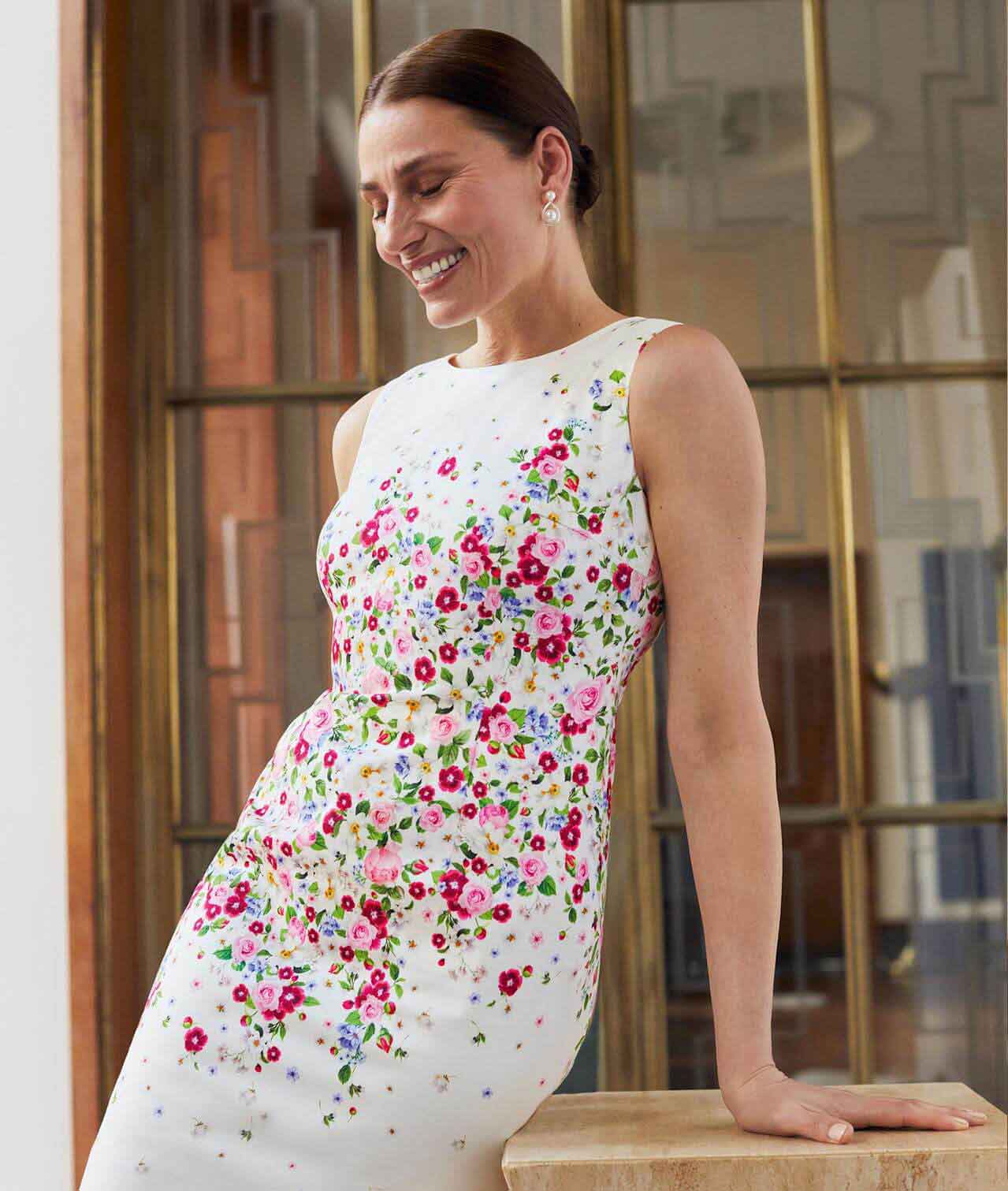 Hobbs model walks through the Riba building wearing a sage green mother of the bride outfit including matching dress, jacket, fascinator and clutch bag.